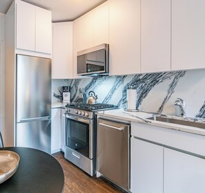 Una cocina moderna con electrodomésticos de acero inoxidable, salpicadero de mármol y armarios blancos.
