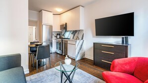 A modern living room with a red sofa, a glass coffee table, and a flat-screen TV mounted on the wall. - Classic NYC Living | UES, Pet-Friendly (New York)