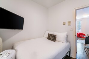 A bedroom with a bed, a flat-screen TV, a heater, and a red chair in the adjacent room.