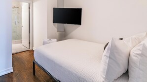 A bedroom with a bed, a television mounted on the wall, a door leading to a bathroom, and a small bedside table. - Classic NYC Living | UES, Pet-Friendly (New York)