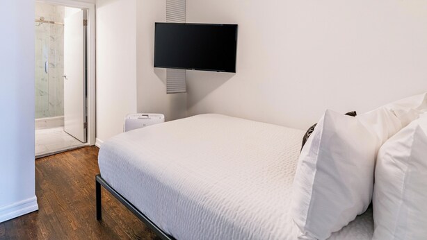 Een slaapkamer met een bed, een aan de muur bevestigde televisie, een deur naar een badkamer en een klein nachtkastje.