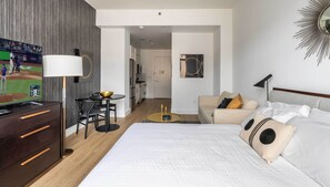 A hotel room with a bed, a desk with a bowl, a chair, a lamp, and a TV displaying a baseball game. - Stunning Greenwich Village Studio with Amenities (New York)
