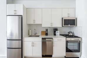 A modern kitchen with stainless steel appliances, white cabinetry, and a tiled backsplash.