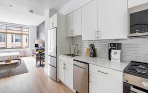 Una cocina moderna con armarios blancos, lavavajillas integrado, cafetera y estufa a gas.