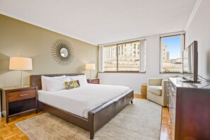 Habitación de hotel con una cama grande, un escritorio, una silla, un televisor y vistas a la ciudad.