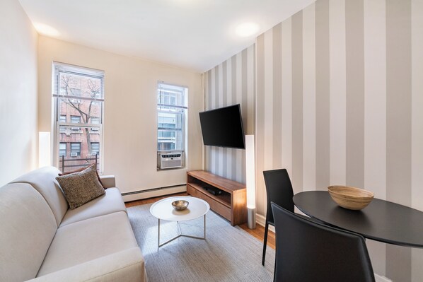 A modern living room with a sofa, a coffee table, a TV, and a dining area.