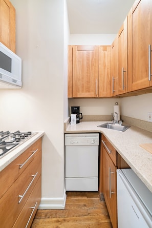 Une cuisine compacte avec des meubles en bois, un lave-vaisselle blanc, une cuisinière et une machine à café.
