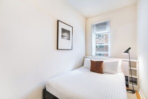 A bedroom with a bed, a window, a picture on the wall, and a floor lamp.