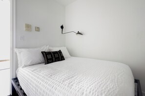 Une chambre à coucher avec un lit, du linge de lit blanc, une lampe noire et une fenêtre.