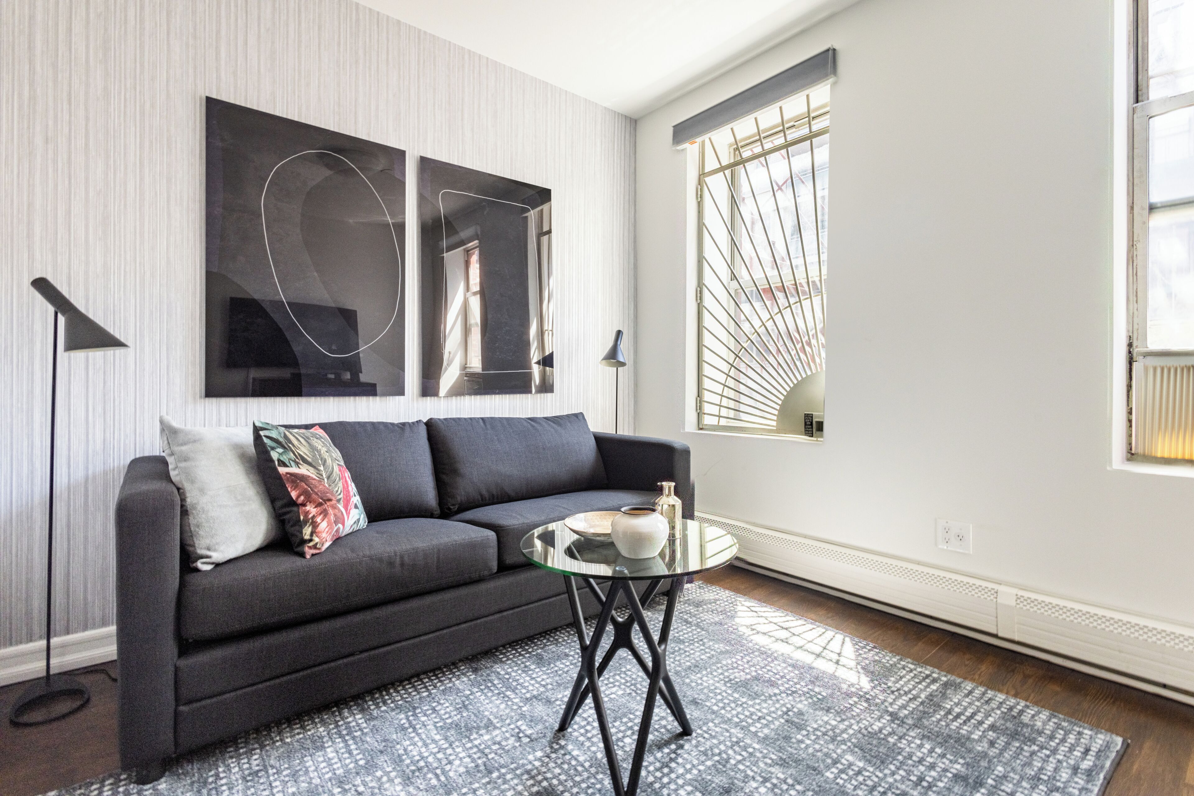 Ein modernes Wohnzimmer mit einem dunkelgrauen Sofa, einem Glastisch und abstrakter Wandkunst.
