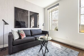 A modern living room with a dark grey sofa, a glass coffee table, and abstract wall art.