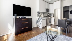 Een moderne keuken met een flatscreen-tv, een donker houten kast, een marmeren achterwand, roestvrijstalen apparatuur en een eethoek met een glazen tafel en stoelen.