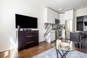 Una cocina moderna con televisor de pantalla plana, gabinete de madera oscura, salpicadero de mármol, electrodomésticos de acero inoxidable y una zona de comedor con mesa y sillas de vidrio.