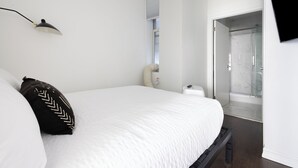 Een moderne slaapkamer met een groot bed, een nachtkastje, een lamp en een douchegedeelte zichtbaar door een glazen deur.