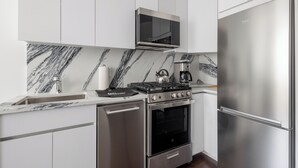 Een moderne keuken met witte kasten, een roestvrijstalen koelkast, een inbouwoven, een magnetron en een gasfornuis.