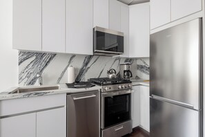 Una cocina moderna con gabinetes blancos, un refrigerador de acero inoxidable, horno empotrado, microondas y estufa a gas.