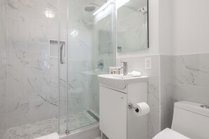 A modern bathroom with a glass-enclosed shower, a white sink with a mirror above it, and a toilet.