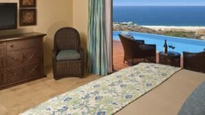 Un dormitorio con una ventana grande que da a una playa, una cama, un aparador y una silla.