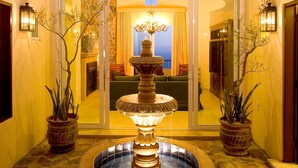 Un patio con una fuente central, plantas en macetas y vista a una habitación con candelabro.