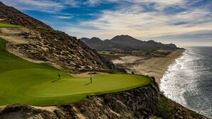 Un campo de golf costero con vistas al océano y montañas al fondo.