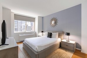 Un dormitorio moderno con una cama grande, mesitas de noche, un espejo y vistas a la ciudad desde la ventana.