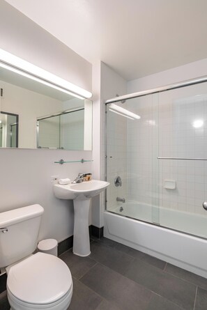 Un baño moderno con inodoro, lavamanos pedestal y ducha con mampara de vidrio.