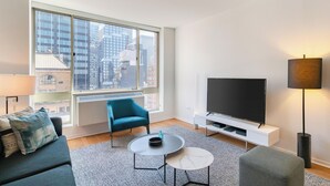 Ein modernes Wohnzimmer mit einem großen Fenster, einem Flachbildfernseher, einem blauen Sessel, einem grauen Sofa und einem kleinen Couchtisch.