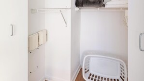 Ein kleiner, weißer Kleiderschrank mit Regalen, einer Kleiderstange und einem Wäschekorb.