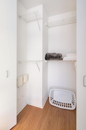 A small, white closet with shelves, a hanging rack, and a laundry basket. - Broadway Area Living | Midtown West, Pet-Friendly (New York)