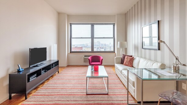 A modern living room with a flat-screen TV, a glass coffee table, a red chair, a white sofa, and a striped wall.