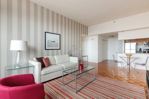 Una sala de estar moderna con un sofá blanco, una mesa de centro de vidrio y una silla roja. Hay una alfombra a rayas en el suelo.