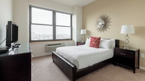 A bedroom with a large window, a bed, a TV, and a desk.