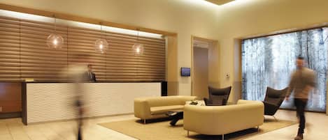 A modern lobby with a reception desk, seating area, and a large window with a forest view.