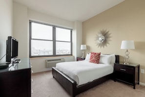 A bedroom with a large window, a bed, a TV, and a desk.