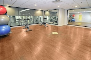 Une salle de sport équipée de matériel d’exercice, dotée d’un mur entièrement recouvert de miroirs et d’un plancher en bois.