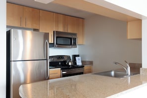 A modern kitchen with stainless steel appliances, wooden cabinets, and a granite countertop.