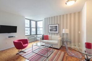 A modern living room with a glass coffee table, a red chair, a white sofa, and a striped rug.