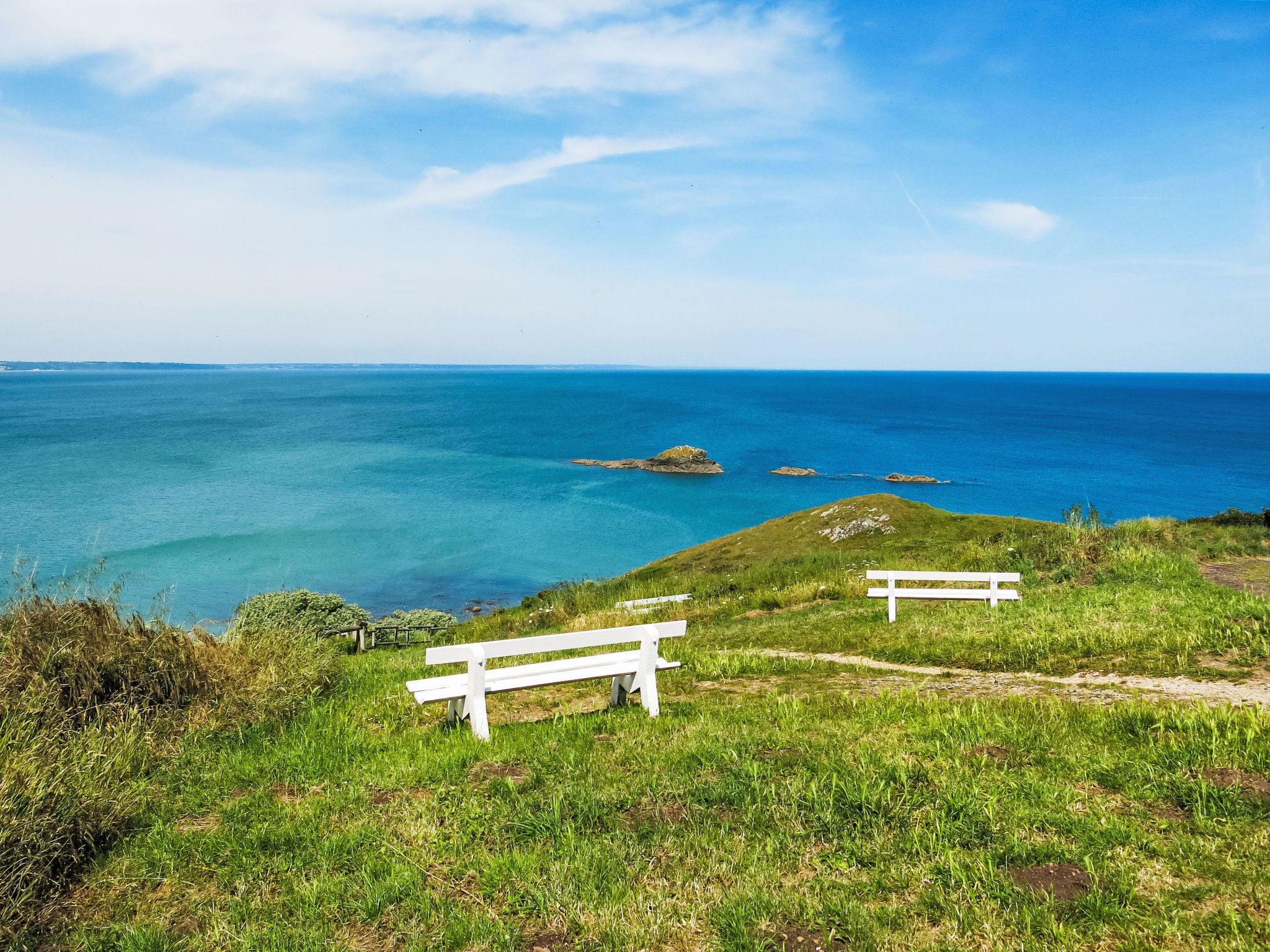 Un paysage côtier avec deux bancs blancs donnant sur la mer.