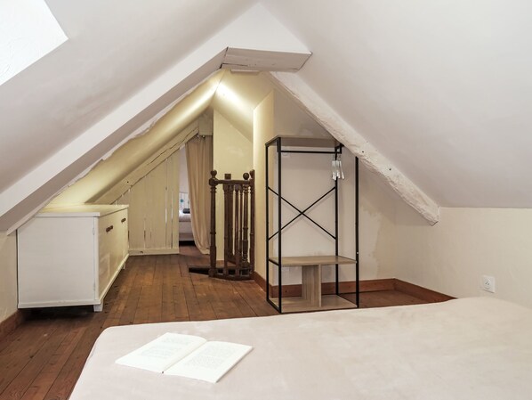 A narrow attic bedroom with a sloped ceiling, a wooden floor, a white bed, and a metal shelf unit.