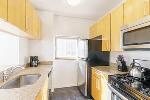A kitchen with wooden cabinets, a stainless steel sink, a refrigerator, a stove, and a window.