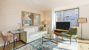 A modern living room with a white sofa, a glass coffee table, a green armchair, a TV, and artwork on the wall. - Centrally Located Chelsea Luxe One Bedroom (New York)