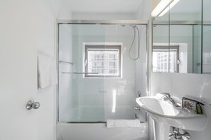 Un baño moderno con ducha de vidrio, lavamanos blanco y un espejo grande.