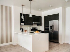 A modern kitchen with a central island, dark cabinetry, stainless steel appliances, and a striped wall pattern. - Modern One Bedroom in Silicon Valley (Sunnyvale)