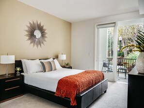 Un dormitorio moderno con una cama grande, dos mesitas de noche, un espejo decorativo y vistas al exterior a través de una puerta corredera de vidrio.