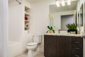 Un baño moderno con inodoro blanco, tocador de madera oscura y un espejo grande.