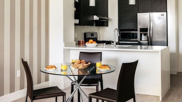 A modern kitchen with a central island, black cabinets, stainless steel appliances, and a dining area with a glass table and black chairs. - Silicon Valley One Bedroom with Terrace (Sunnyvale)