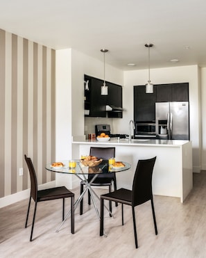 A modern kitchen with a central island, black cabinets, stainless steel appliances, and a dining area with a glass table and black chairs.