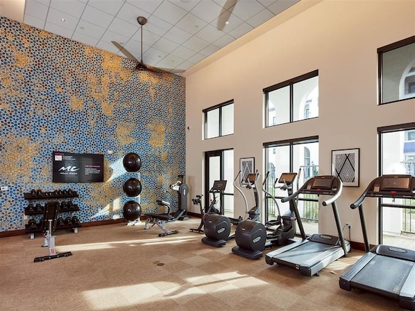 A gym with treadmills, elliptical machines, and stationary bikes, a large mirror, and a television on the wall.
