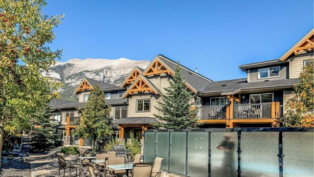 Un complejo turístico con varias construcciones de estilo chalete, asientos al aire libre y montañas al fondo.