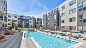 A swimming pool with lounge chairs and a barbecue area, surrounded by modern buildings.
